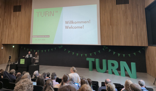 Blick von den oberen Rängen in einem großen Saal auf die Bühne und das sitzende Publikum
