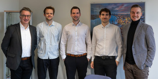 Die drei neuen Mitarbeiter und die Institutsleitung stehen vor einer Wand in einem Besprechungsraum