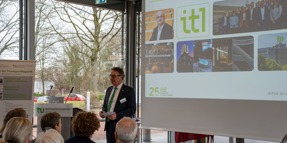 Professor Uwe Clausen steht vor einer Leinwand und spricht vor Publikum