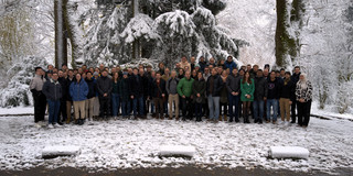 Personen haben sich vor einem Wald mit Schnee zu einem Gruppenbild aufgestellt