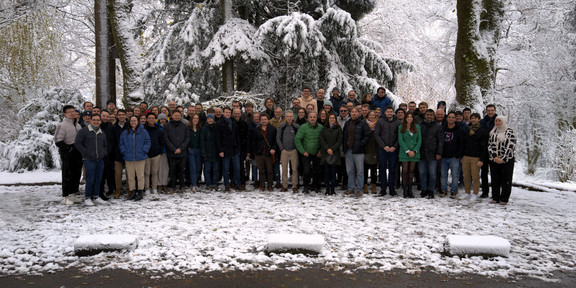 Personen haben sich vor einem Wald mit Schnee zu einem Gruppenbild aufgestellt