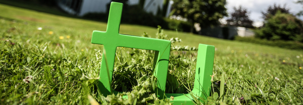 Im Vordergrund steht das TU Logo im Gras, im Hintergrund das Audimax.