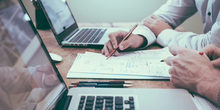 Zweipersonen arbeiten an einem Text zwischen zwei Laptops