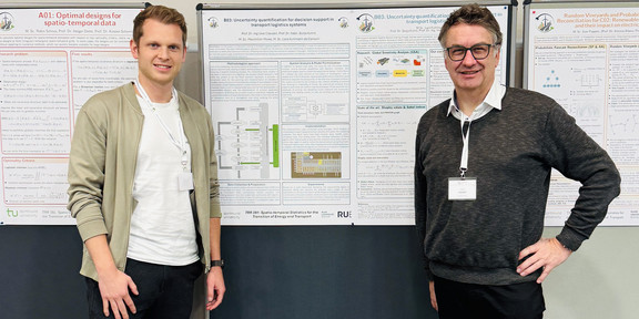 Professor Clausen und Herr Mowe stehen vor einer Pinnwand mit einem Poster