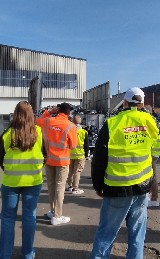 Die Mitarbeitenden des ITL stehen in Warnweste auf einem Platz der Recyclinganlage. Dazwischen steht Herr Michalski und erklärt etwas