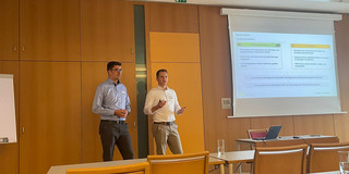 Zwei Personen vor einer Leinwand halten eine Präsentation