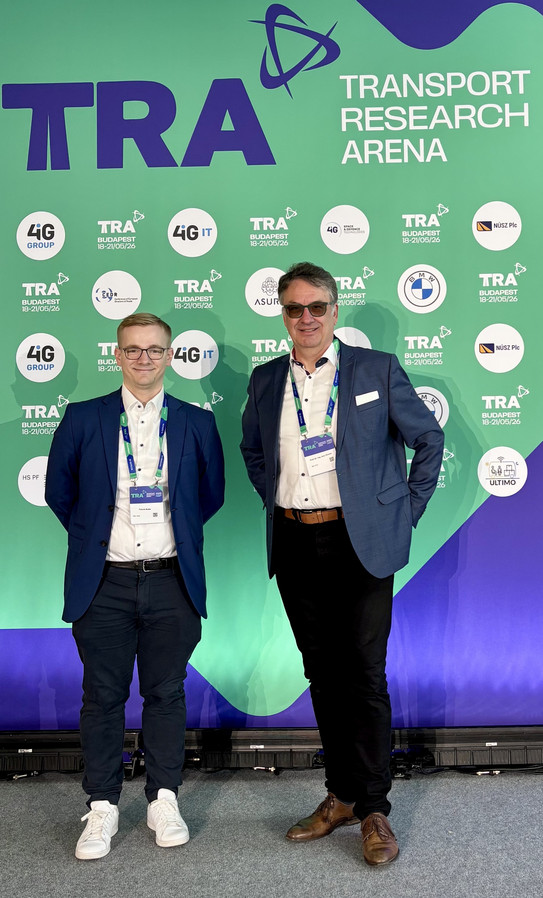 Professor Clausen und Patrick Buhle stehen vor einer TRA Werbewand