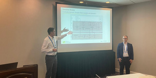 Herr Jurgeleit und Herr Buhle vor einer Präsentationstafel. Herr Jurgeleit zeigt auf das Bild.