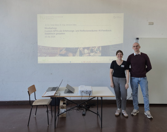 Tanja Nebel und Clemens Balke stehen vor einer Wand auf der die Titelfolie eine Präsentation projeziert wird