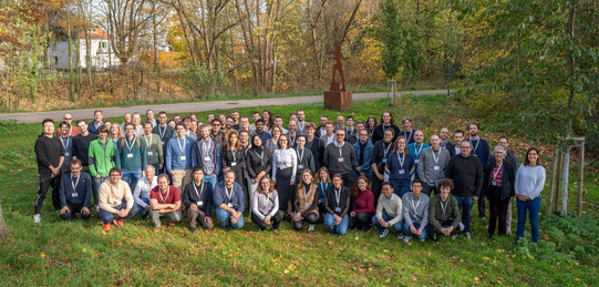 Eine Gruppe an Menschen steht auf einer Wiese und blickt in die Kamera