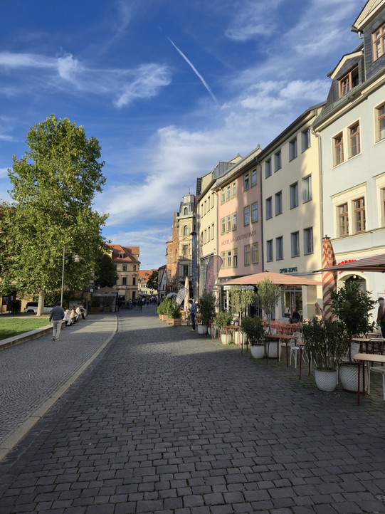 Blick auf eine historische Straße mit alten Häusern in Weimar. Im Vordergrund stehen Schirme und Tische der Gastronomie.