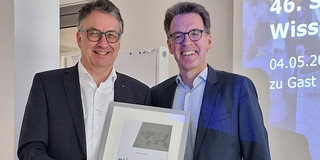 Professor Clausen steht neben Dr. Thorsten Schmidt und hält eine eingerahmte Auszeichnung in der Hand