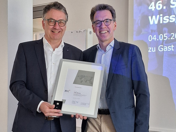 Professor Clausen steht neben Dr. Thorsten Schmidt und hält eine eingerahmte Auszeichnung in der Hand